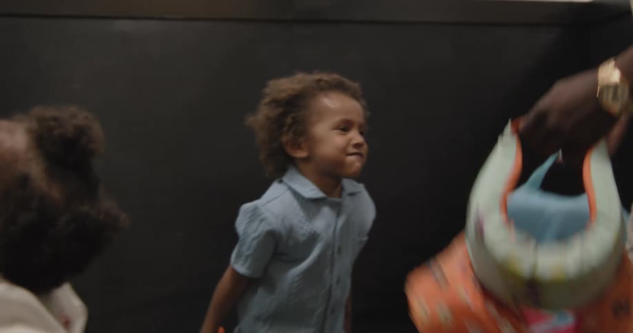A happy family with two young kids laughs and plays together in slow motion indoors