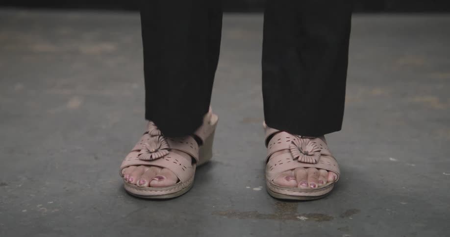 Close-up shot of a woman's feet in pink open-toed wedge sandals tapping impatiently on a concrete floor
