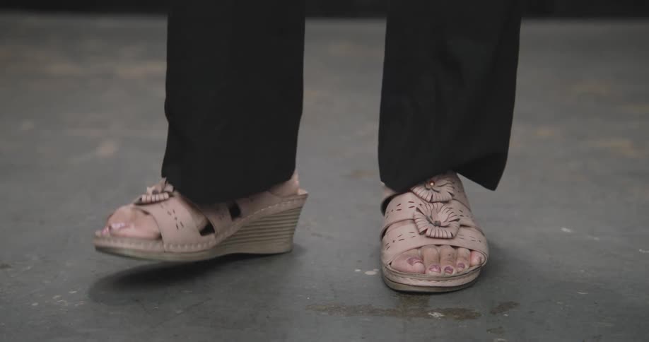 A close-up shot of a person's feet in pink sandals tapping impatiently on a concrete floor