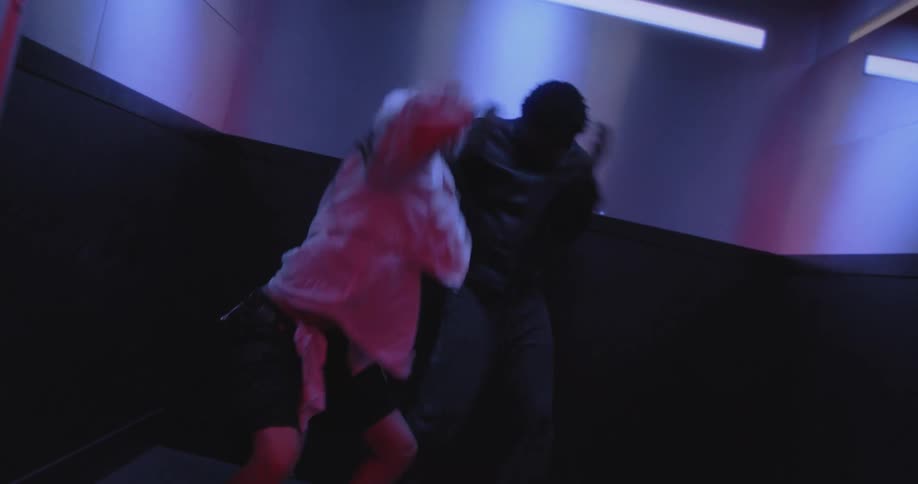A man and a woman perform a high-energy dance routine inside an elevator in a hallway with dramatic red lighting
