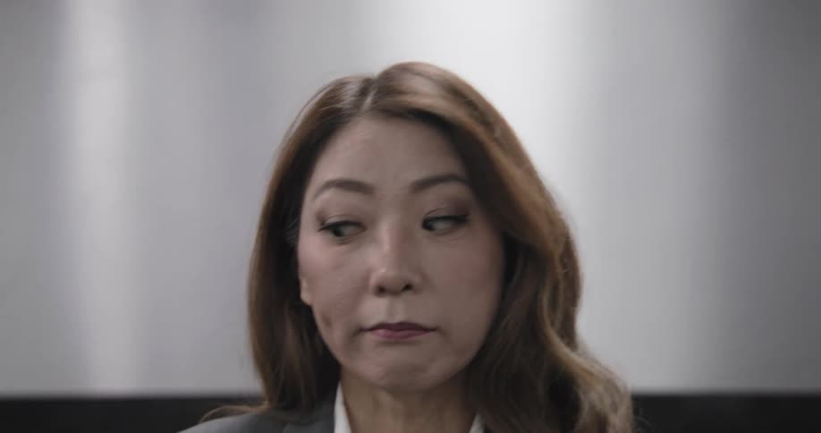 Close-up of a professional Asian woman looking around with a concerned expression before walking out of the frame