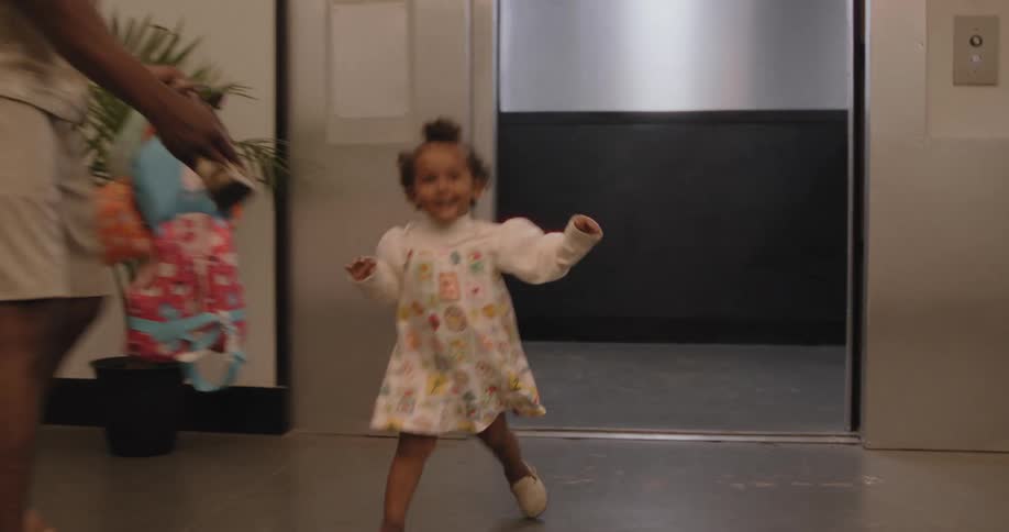 An adorable little girl with a big smile runs out of an elevator in slow motion, followed by her father