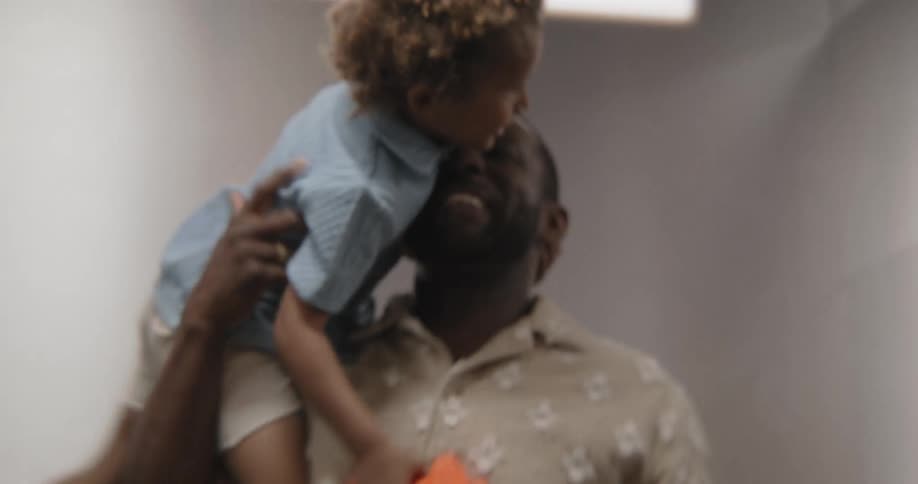 A loving Black father laughs and plays with his young son, carrying him on his shoulders and then in his arms in slow motion