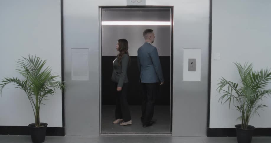 A businessman and a businesswoman meet in a minimalist lobby and take an elevator together as the doors close