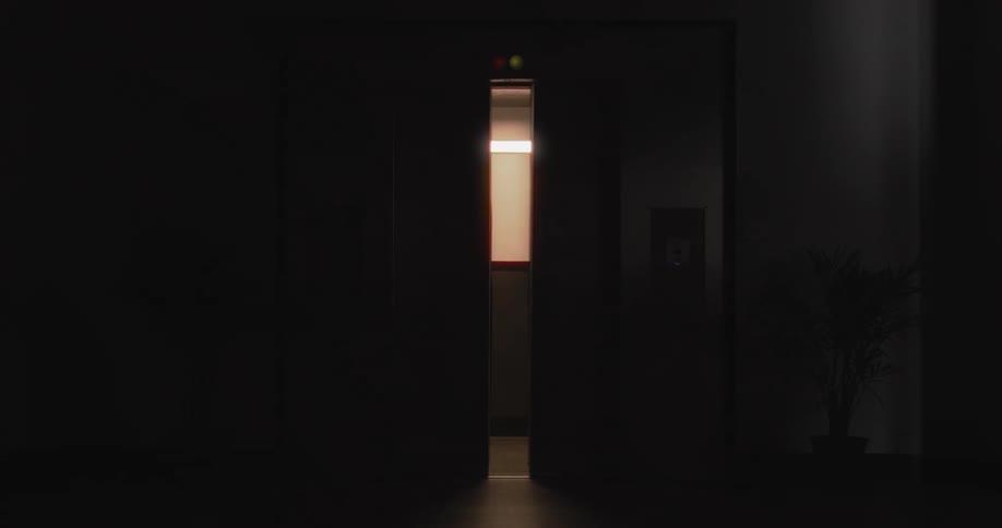 The doors of an empty, lit elevator slowly close in a dark hallway, leaving the scene in complete darkness