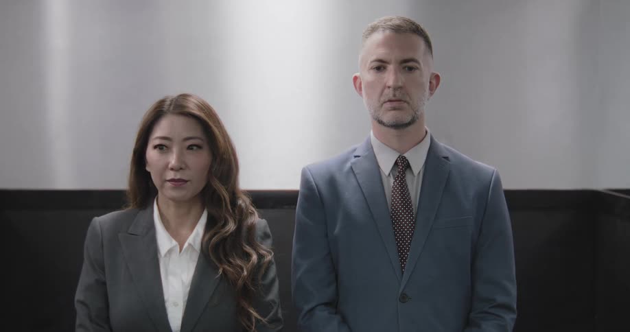 A businessman and businesswoman in suits stand in awkward and tense silence after receiving bad news