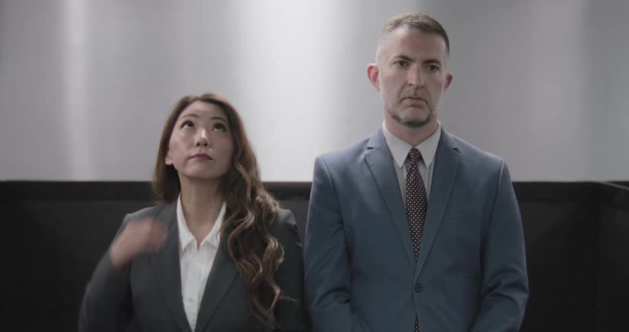 A businessman and a businesswoman ride awkwardly in an elevator together
