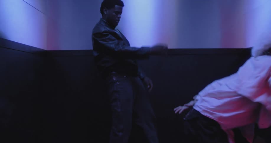 Stylish man and woman dance together in slow motion inside a room with cool blue neon lighting