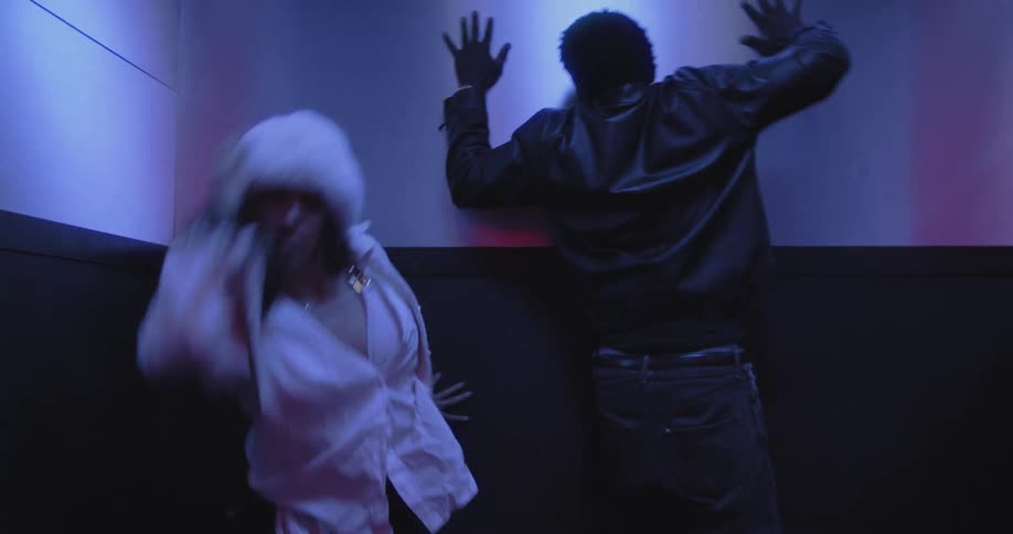 Two dancers perform a modern and energetic routine inside an elevator with dramatic red and blue lighting