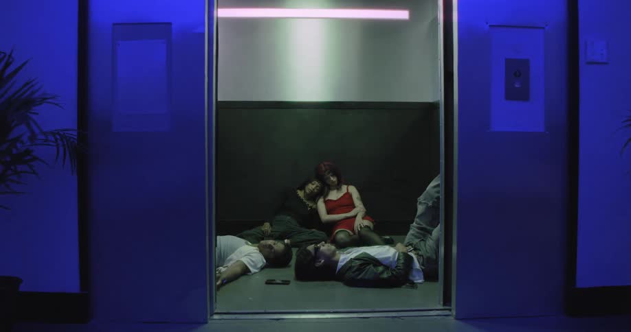 An elevator door opens to reveal a group of young friends asleep on the floor, exhausted after a night out