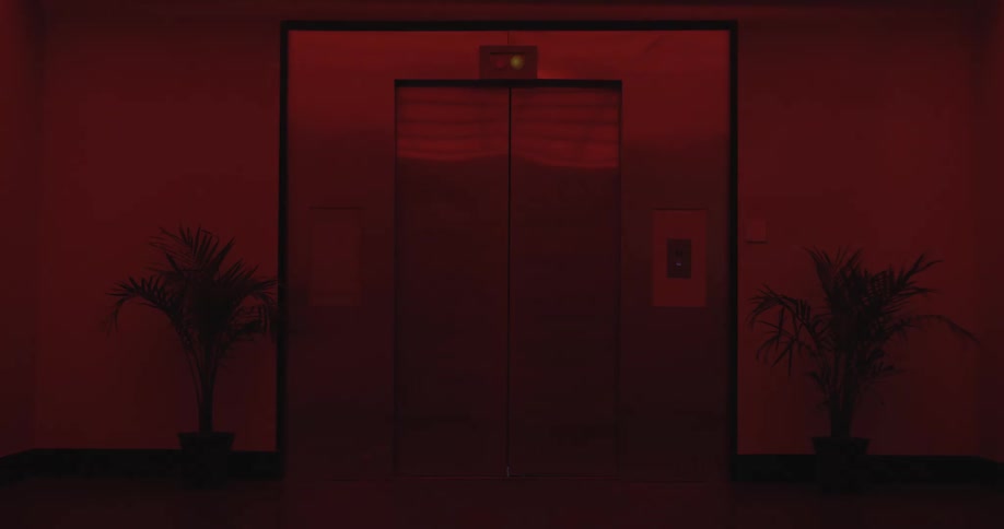 Mysterious elevator doors close in a dark, red-lit hallway