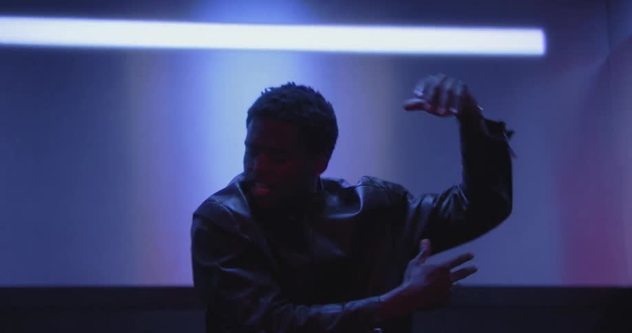 A talented young Black man performs an expressive dance inside an elevator bathed in contrasting red and blue light