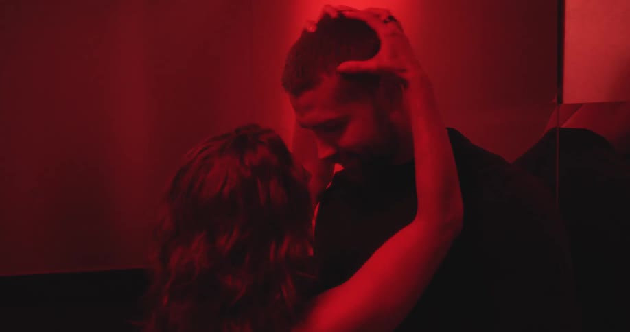 A passionate couple embraces and shares an intimate moment in a dark room with dramatic red lighting