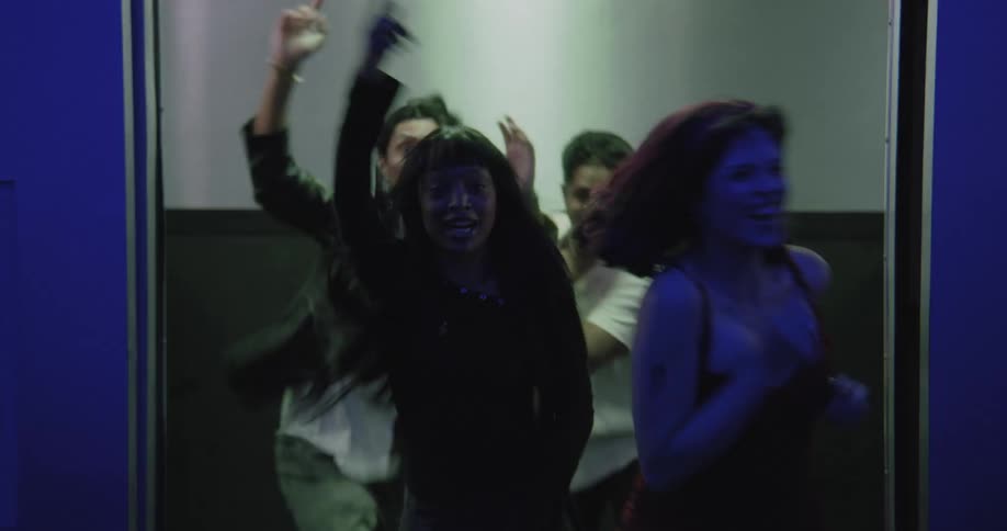 As blue elevator doors open, a group of four energetic friends dance out into a hallway