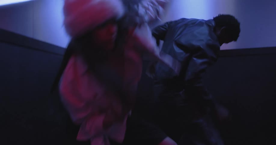 A man and woman perform an expressive and energetic freestyle dance inside a moody, neon-lit elevator