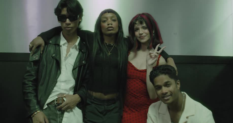 A diverse group of four stylish young friends strike poses for the camera inside a moody, green-lit elevator