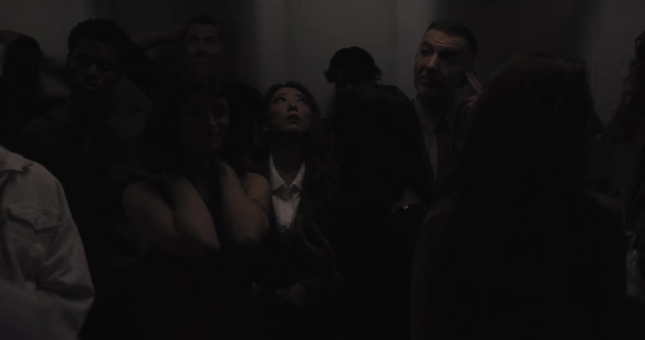 A diverse crowd of anxious people are stuck together in a crowded elevator as the lights flicker on and off