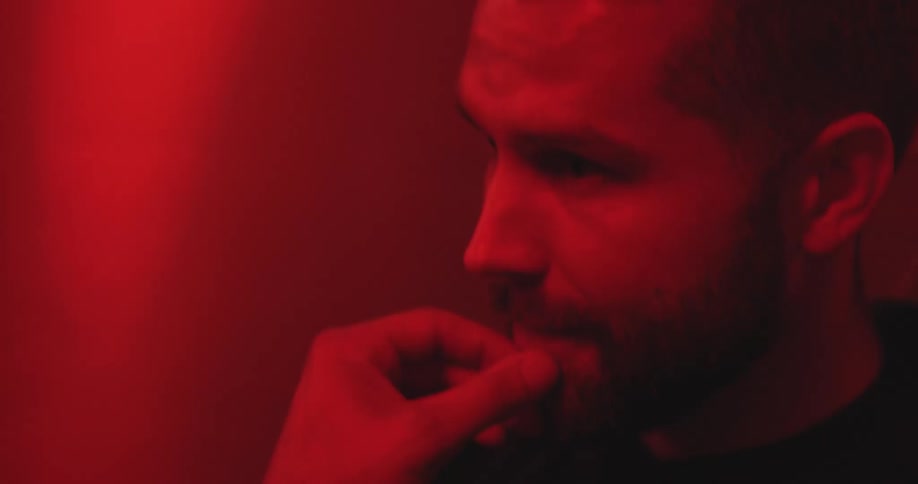 A mysterious bearded man thinks deeply in a dark room with dramatic red lighting, ending with a subtle smile