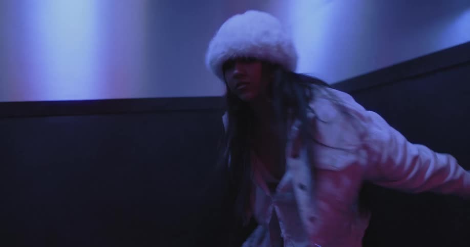 A stylish man and woman perform a powerful and expressive dance routine in slow motion inside a small, futuristic room with moody neon lighting