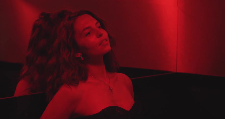A stylish woman in a black dress poses thoughtfully in a dark room illuminated by a mysterious red light