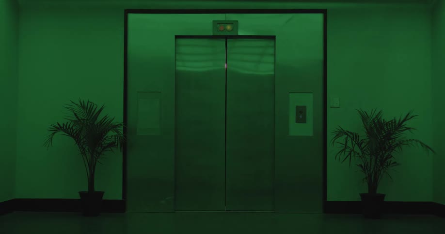 An open elevator door slowly closes in a mysterious, green-lit hallway