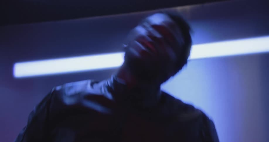 A young Black man dances with expressive energy in a room illuminated by a single blue light