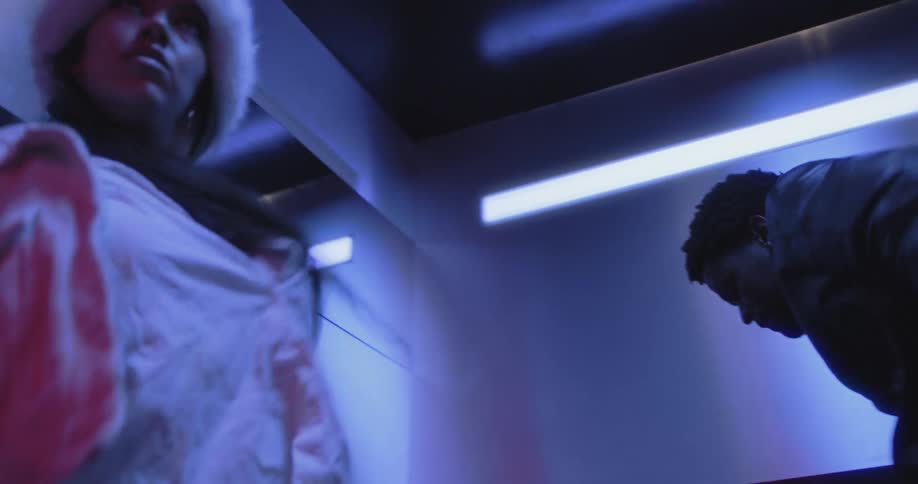 A dynamic slow-motion push-in shot captures two energetic dancers performing inside a neon-lit elevator