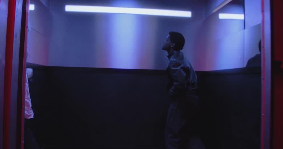 A fashionable young couple dances expressively into an elevator with dramatic red and blue lighting as the doors close