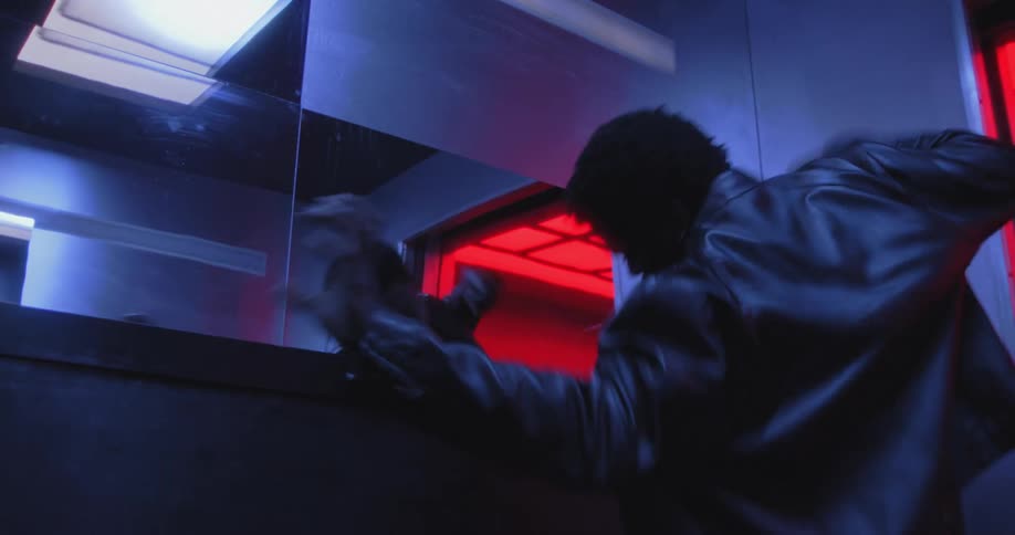 An anguished man dances wildly in a mirrored elevator, wrestling with his inner turmoil under intense red and blue lights
