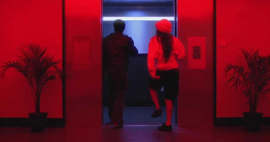 Slow motion of a stylish man and woman dancing energetically into an elevator in a dark corridor with vibrant red lighting