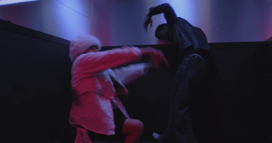 A slow push-in shot reveals a man and woman performing an intense contemporary dance inside an elevator illuminated by moody red and blue lights