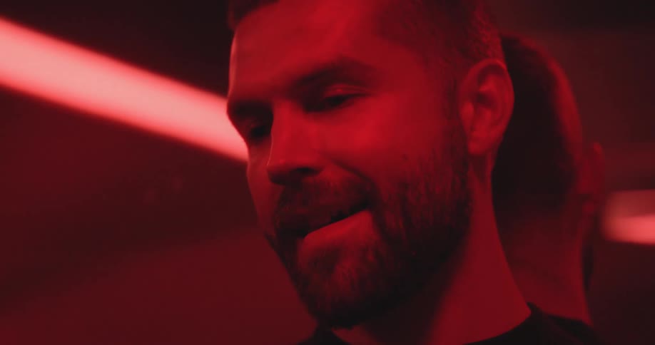 A handsome bearded man smiles subtly as he contemplates in a dark room with dramatic red lighting