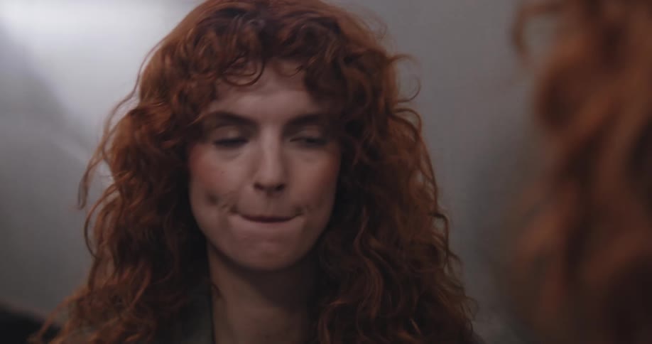 A beautiful redhead with curly hair carefully applies lipstick and fixes her hair while looking at her reflection in the mirror