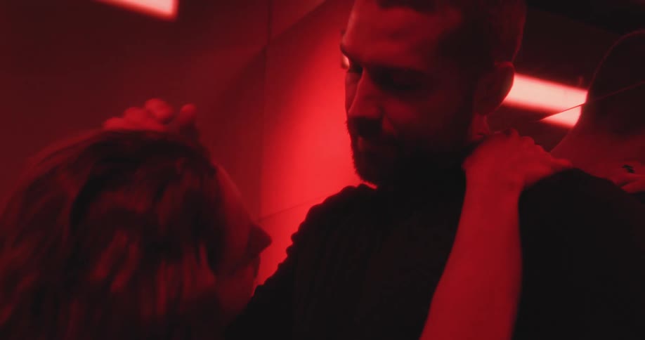 A passionate couple shares an intimate kiss and embrace in a dark, moody room with romantic red lighting