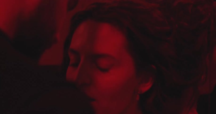A passionate couple embraces intimately in a dark room bathed in a sensual red light