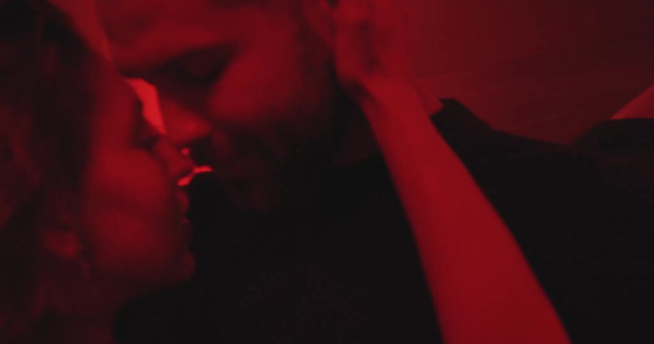 A passionate couple embraces and kisses intimately in a dark room illuminated by dramatic red light
