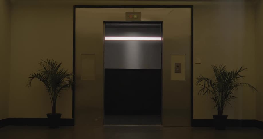 A moody shot of a stainless steel elevator's doors opening and then closing in a quiet, empty hallway