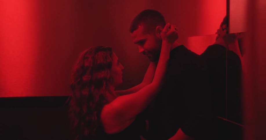 A passionate couple shares an intimate and sensual slow-motion embrace in a room bathed in red light