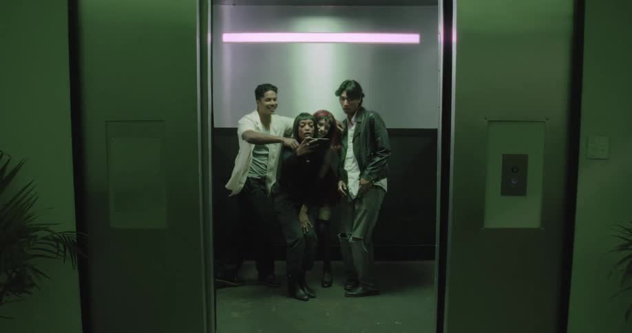 Stylish friends run into an elevator and start an impromptu dance party, taking selfies in the green light