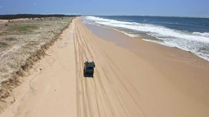 Aerial view of a 4x4 vehicle driving along a remote, sandy beach on a sunny day adventure