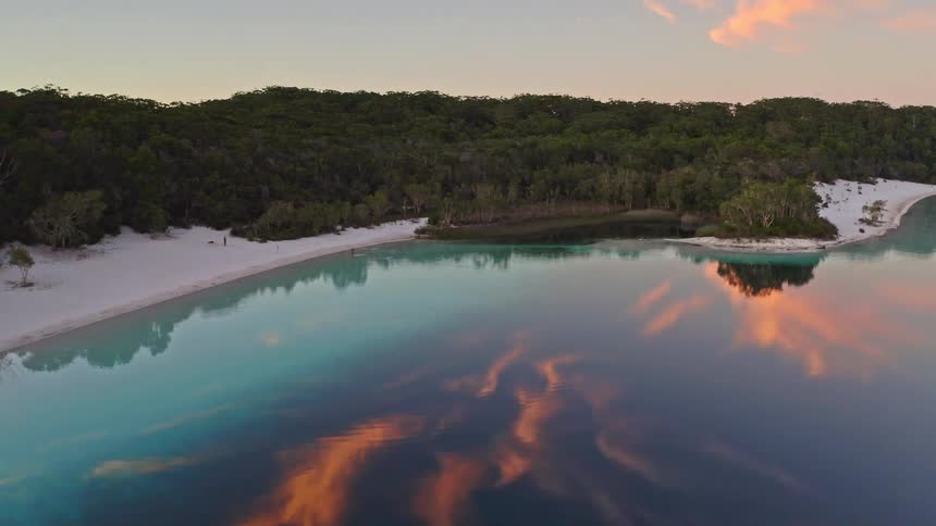 Aerial view of a stunning turquoise lake with a white sand beach, perfectly reflecting the sunset clouds