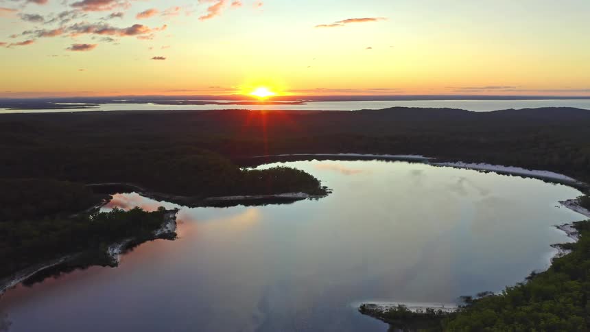 A stunning aerial view captures the golden sunset reflecting on a tranquil lake nestled within a vast, dense forest