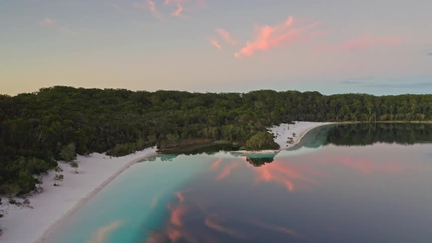 A beautiful aerial view of a serene tropical lake with white sand beaches, reflecting a colorful sunset sky