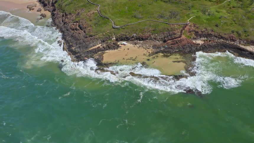 A stunning high-angle aerial view of people swimming in the Champagne Pools on Fraser Island as the camera pulls back to reveal the beautiful coastline