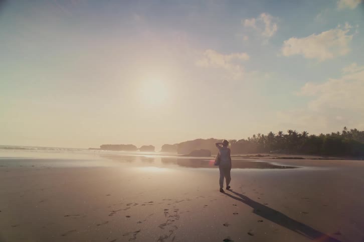 A woman walks in slow motion along a vast, serene tropical beach during a beautiful golden sunset