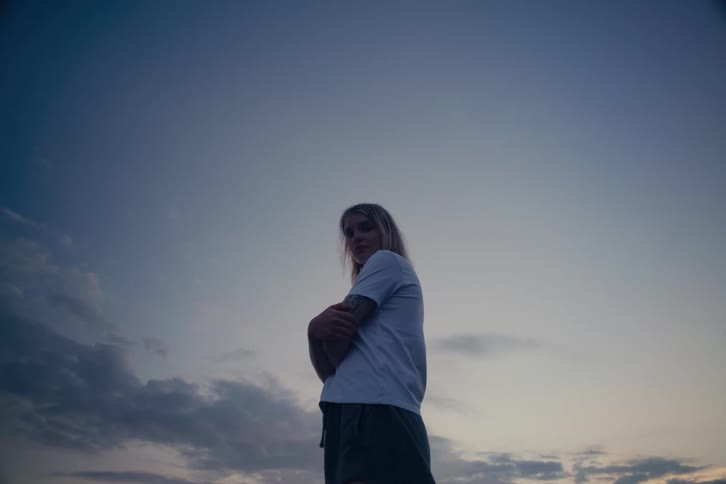 Low angle shot of a pensive woman with crossed arms turning to look at the camera against a beautiful dusky sky