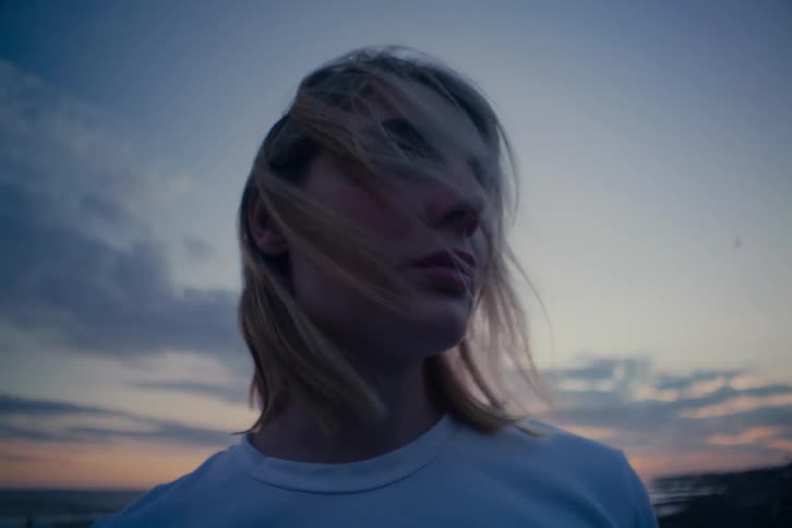 A moody slow-motion portrait of a young woman as the wind blows her hair across her face at dusk