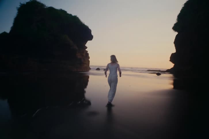 A carefree woman joyfully runs along the wet sand of a secluded beach cove at sunset