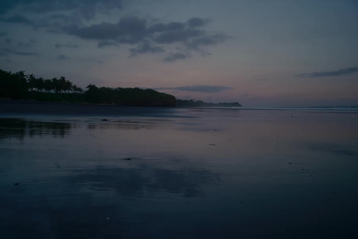 A serene view of a tranquil beach at twilight, with the dark, wet sand reflecting the moody sky