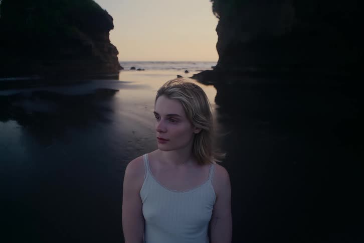 Portrait of a thoughtful young woman with windblown hair on a dark, secluded beach at dusk